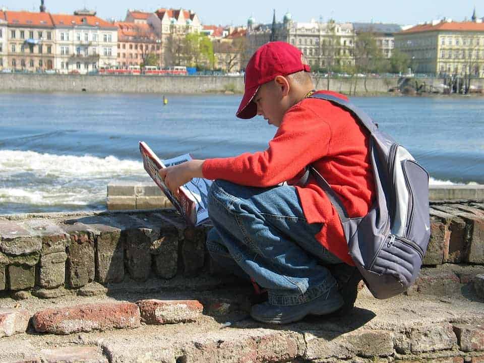 un enfant portant un cartable lit au bord de l'eau